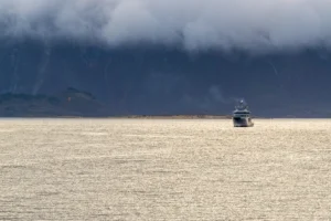 Schip op kalme zee met mistige bergen en lage bewolking op de achtergrond.