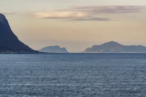Weids zeezicht met kalm water en bergen aan de horizon onder een bewolkte lucht bij zonsondergang