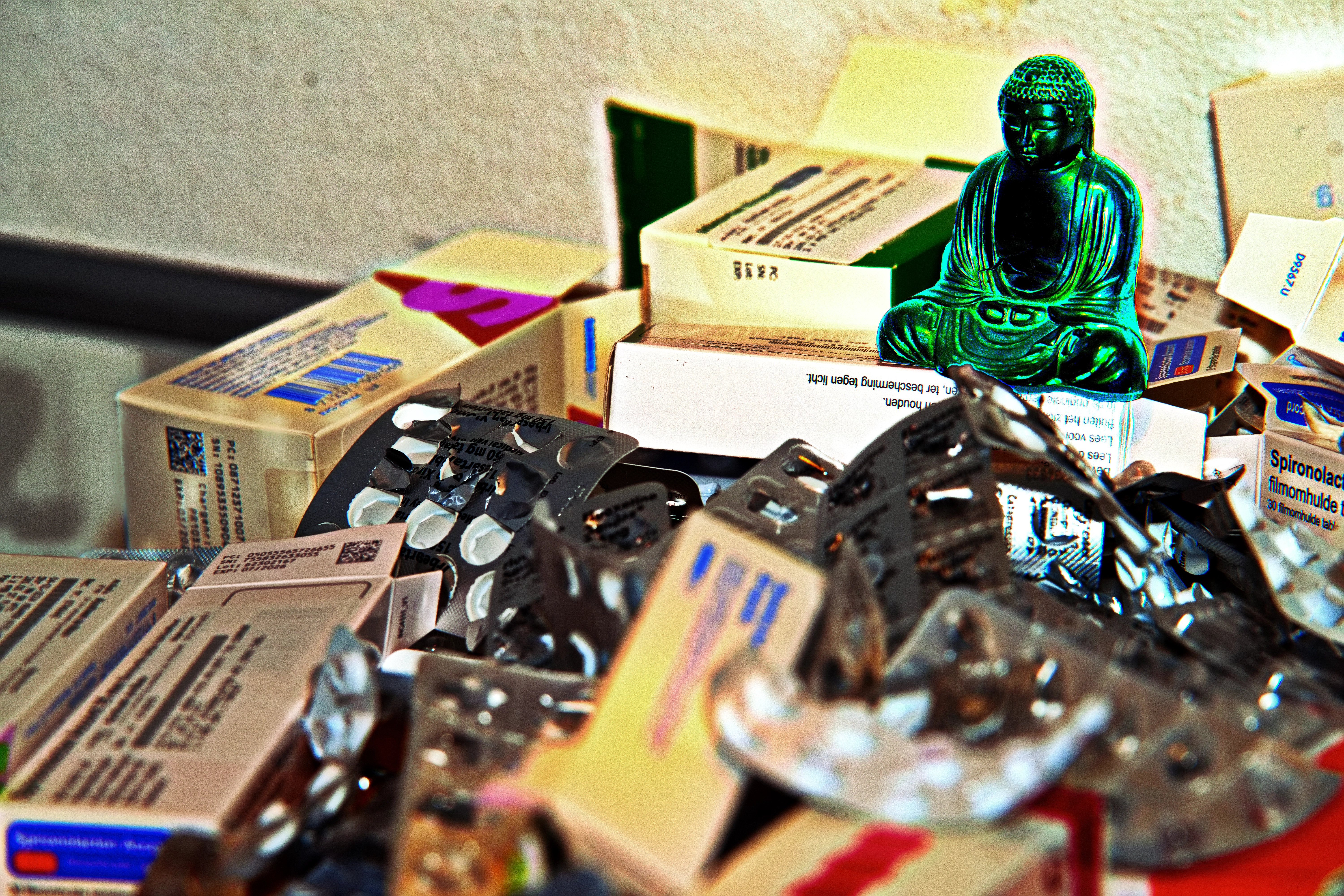 Stapels medicijndozen en lege blisterverpakkingen met een klein Boeddhabeeldje erop.