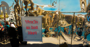 Reflecterende metalen wand met vervormde weerspiegelingen en bord met rode tekst "Vrede in het Hart" (mensen aan tafel op de achtergrond).