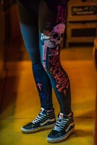 Kleurige legging met skeletkop en teksten, sneakers, staand in warme, onscherpe achtergrond.