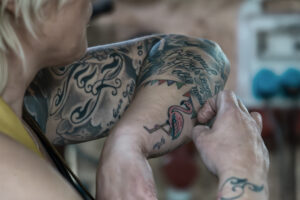 Close-up van iemand met grote tatoeages op armen die een baby vasthoudt, tatoeages met tekst en kleurrijke elementen.